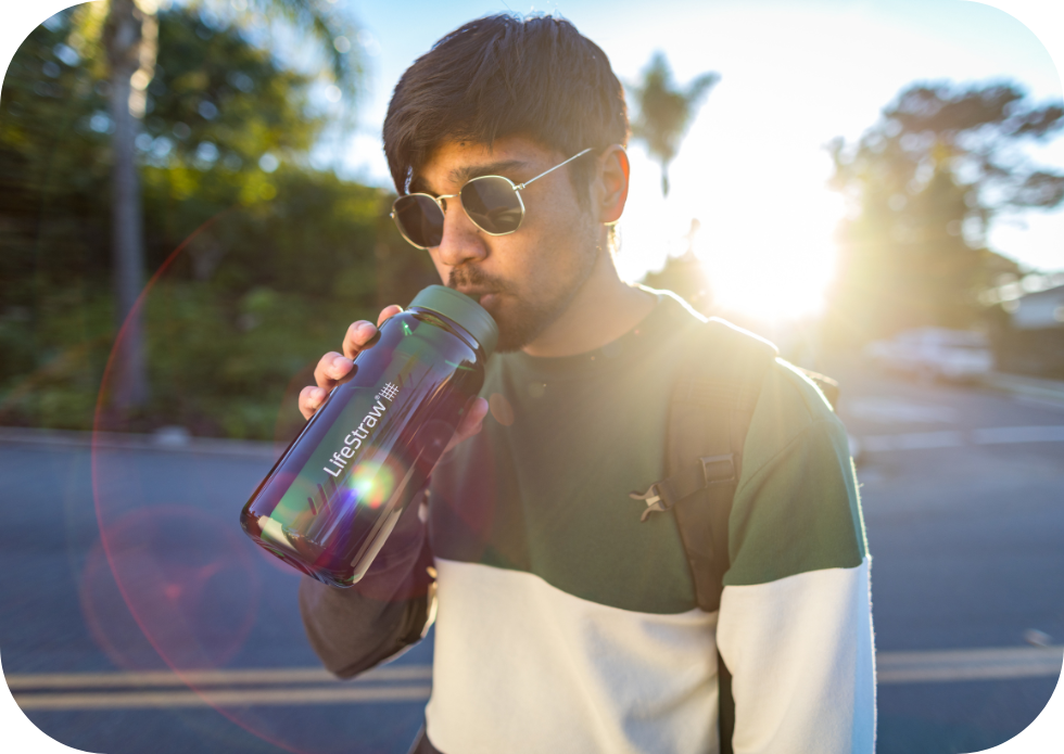 Mężczyzna z plecakiem pije wodę z litrowej butelki LIFESTRAW podczas pieszej wycieczki w pogodny dzień